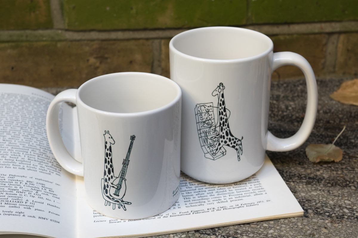 Two mugs, regular and large size, featuring drawings of cartoon giraffes playing musical instruments. On one side, an archlute; on the other, a modular synthesizer.